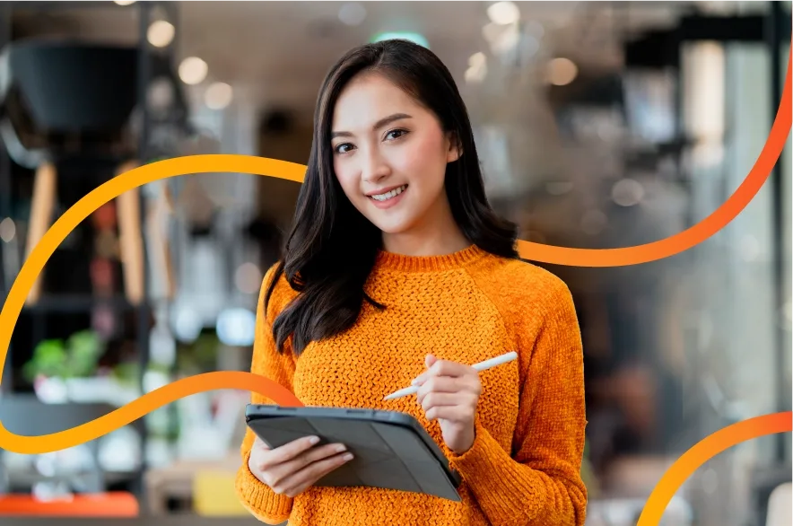 Smiling woman in an orange sweater using a tablet, digital marketing agency Malaysia